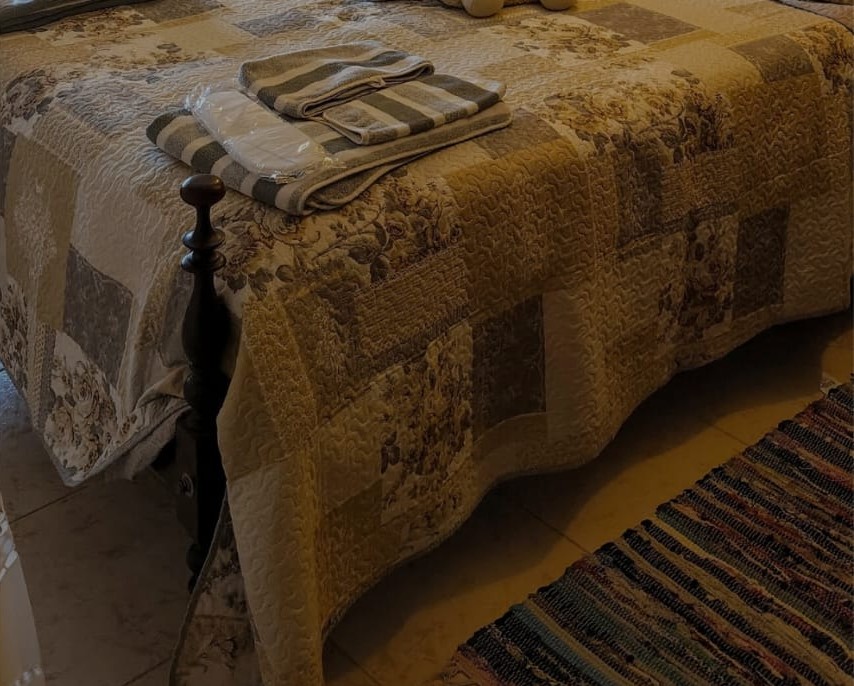 Quarto da AL Casa Pinto, com cama de madeira trabalhada, colcha e toalhas dobradas